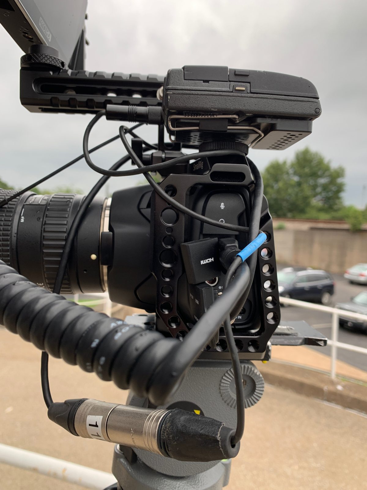 Pocket 6K Pro en cage sur trépied à l'extérieur, avec moniteur, poignée et câble audio XLR.